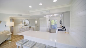 Una cocina moderna con una isla central, un comedor con un espejo redondo y un cartel que dice 'BEACH HOUSE'.