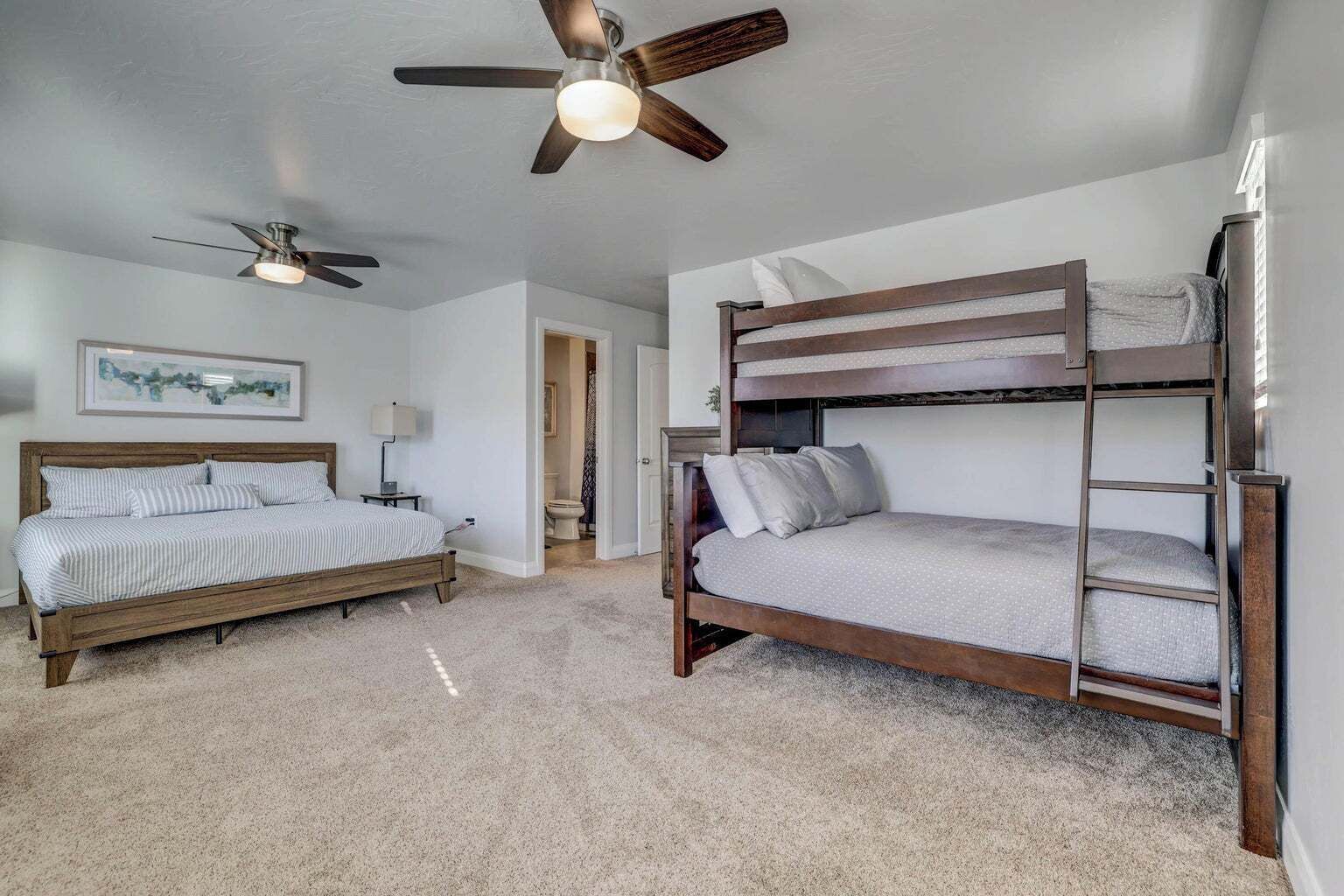 A bedroom with a bunk bed, a single bed, a ceiling fan, and a framed picture on the wall.