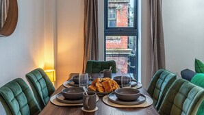 A dining area with a wooden table set for six, surrounded by green upholstered chairs.