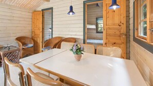 A cozy wooden cabin interior with a dining table, wicker chairs, and a blue hanging light fixture.