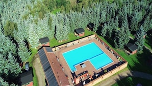 An aerial view of a resort with a large swimming pool, surrounded by trees and small buildings.