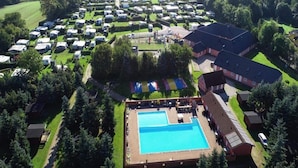 Vue aérienne d’un terrain de camping avec des camping-cars, une piscine et un grand bâtiment.
