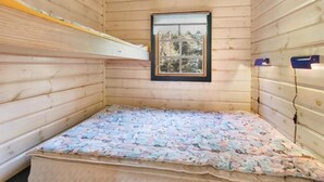 A small, wooden room with a bunk bed, a window with a view of trees, and a wall-mounted shelf.