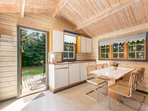 A compact kitchen with a dining area, wooden walls, and large windows. - 4 Person Holiday Park Home in Graested (Graested)
