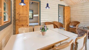 L’intérieur d’un chalet en bois comprend une table à manger, des chaises en osier et deux lampes suspendues.