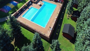 Une grande piscine rectangulaire divisée en deux zones distinctes, entourée d’une pelouse et d’arbres.