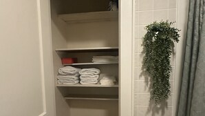 Et smalt walk-in closet med hylder til foldede håndklæder og en hængende plante.