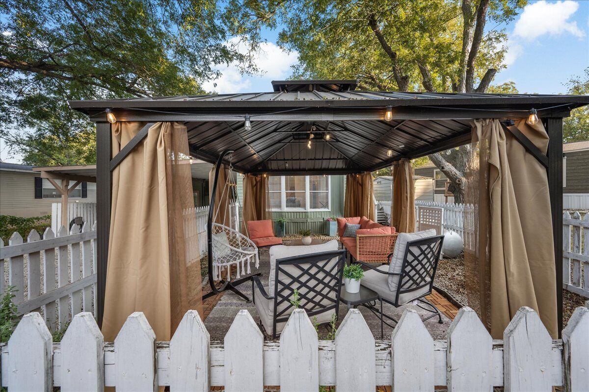 Un espace extérieur aménagé avec une pergola, une clôture en bois peinte en blanc et du mobilier de jardin, le tout abrité.