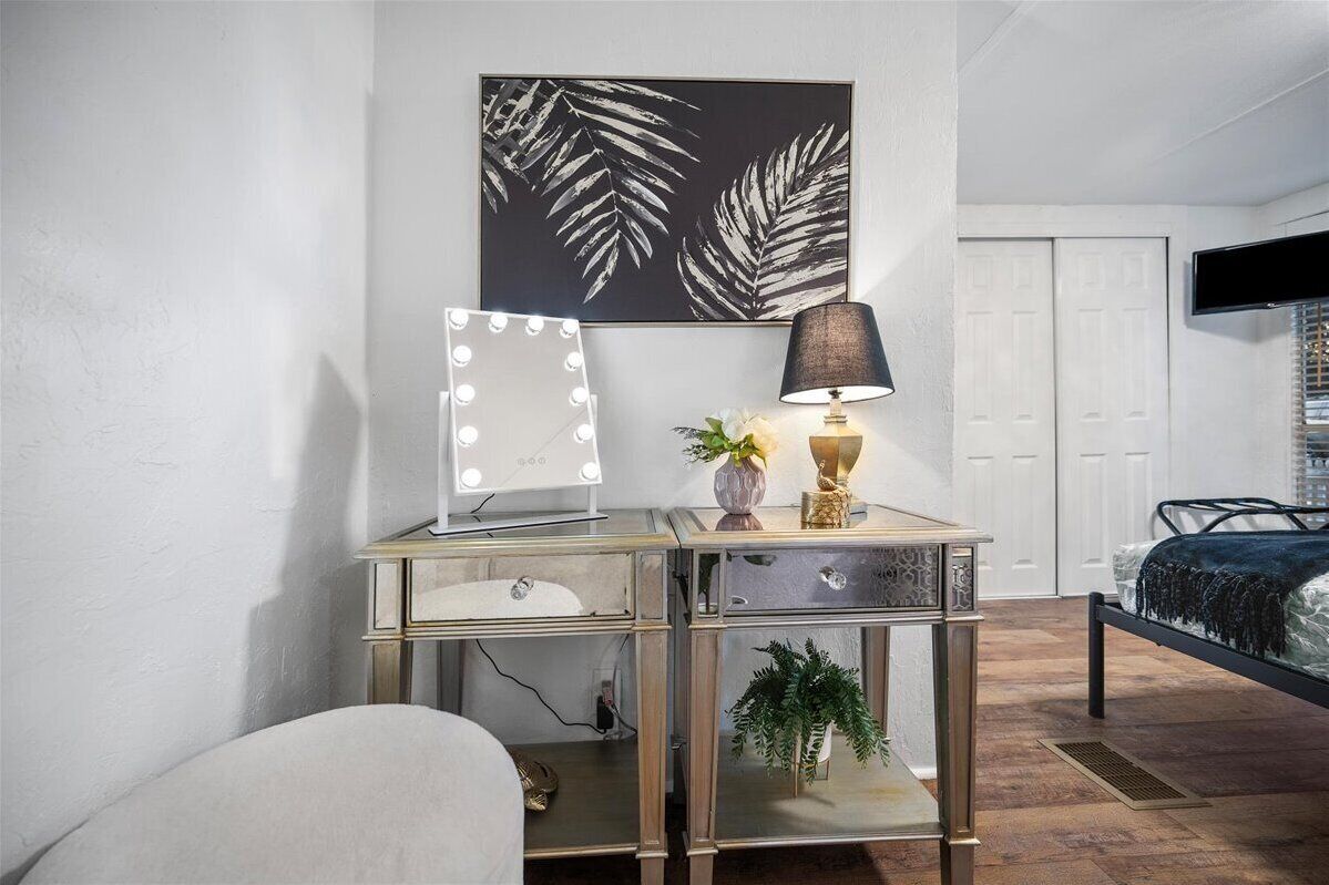Een slaapkamer met een bed, een kaptafel met spiegel en verlichting, een plant en een tv aan de muur.