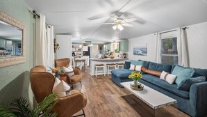 A modern living room with a blue sofa, brown armchairs, a white coffee table, and a ceiling fan. - Hot Tub, Fire pit, Cabana, Covered Patio & Pet-friendly Riverside Retreat (New Braunfels)