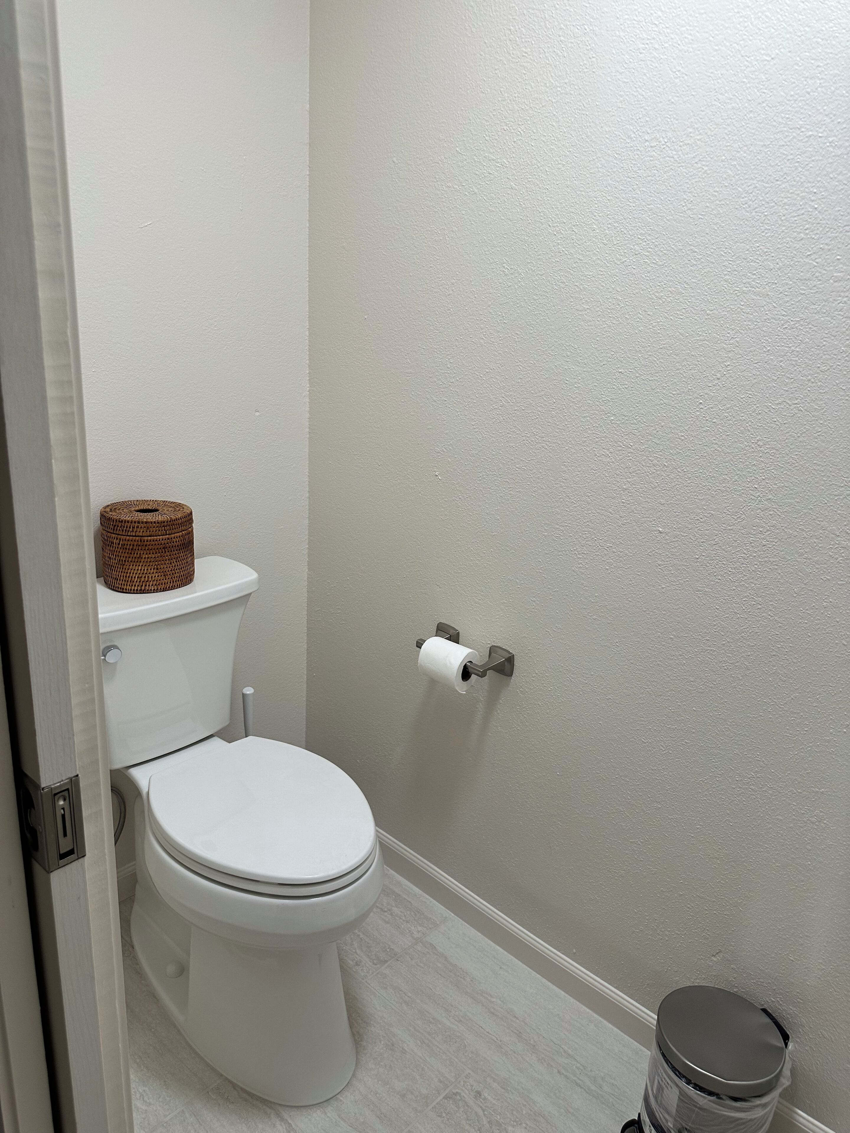 A bathroom with a toilet, a toilet paper holder, and a trash can.