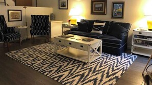 Uma sala de estar com sofá, poltronas, mesa de centro e tapete estampado.