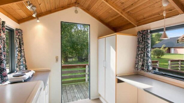 A compact kitchen with a wooden ceiling, a large window with a view of a house, and a door leading to an outdoor area. - Amazing Holiday Home With Terrace (Graested)