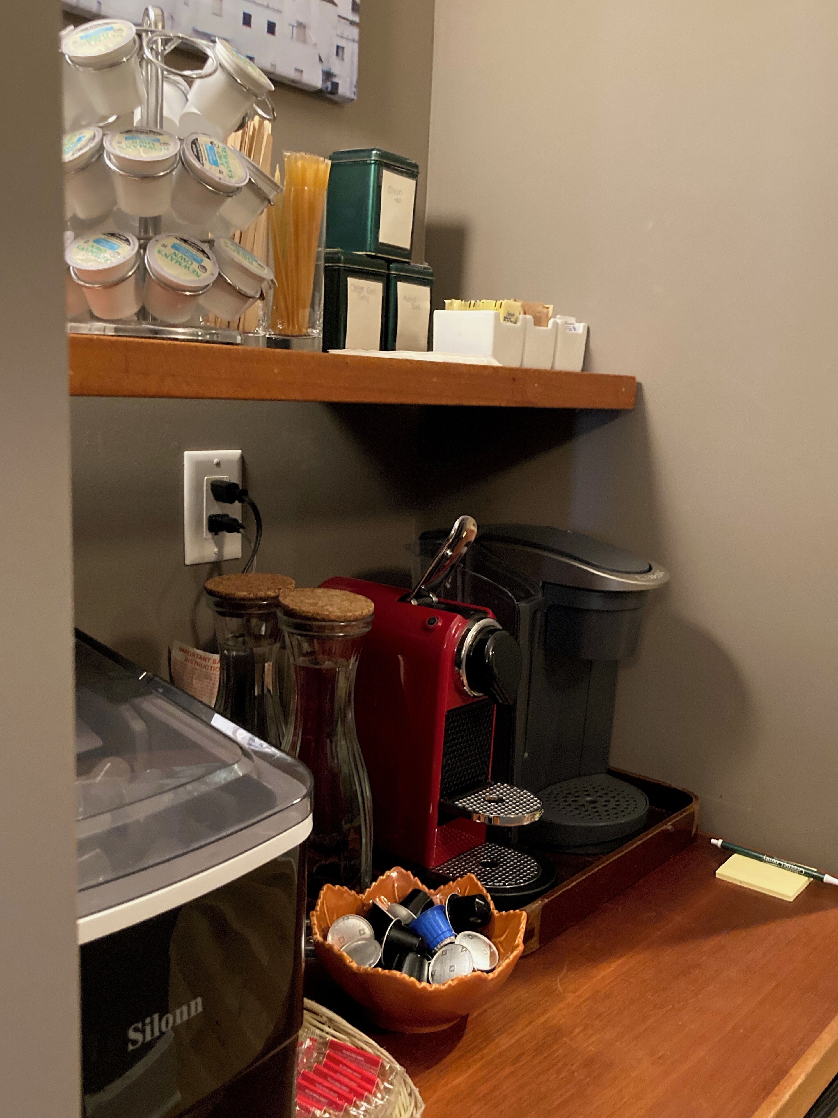 A kitchen area with a coffee maker, jars, and a basket of coffee pods.