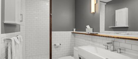 A modern bathroom with a glass shower enclosure, white subway tiles, a white toilet, and a large vanity with a mirror.