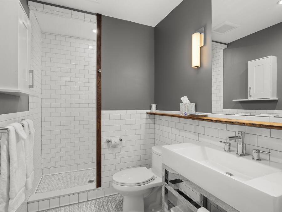 A modern bathroom with a glass shower enclosure, white subway tiles, a white toilet, and a large vanity with a mirror.