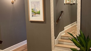 En hall med en trappa, en inramad tavla, en spegel och en krukväxt.