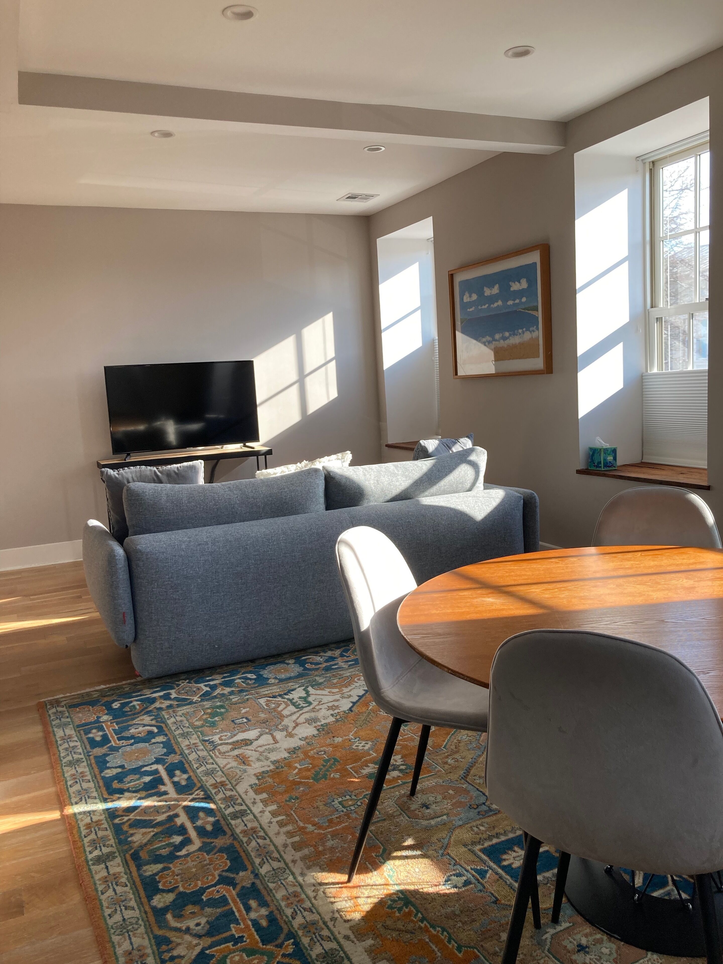 A modern living room with a sofa, a TV, a dining table with chairs, and a patterned rug.