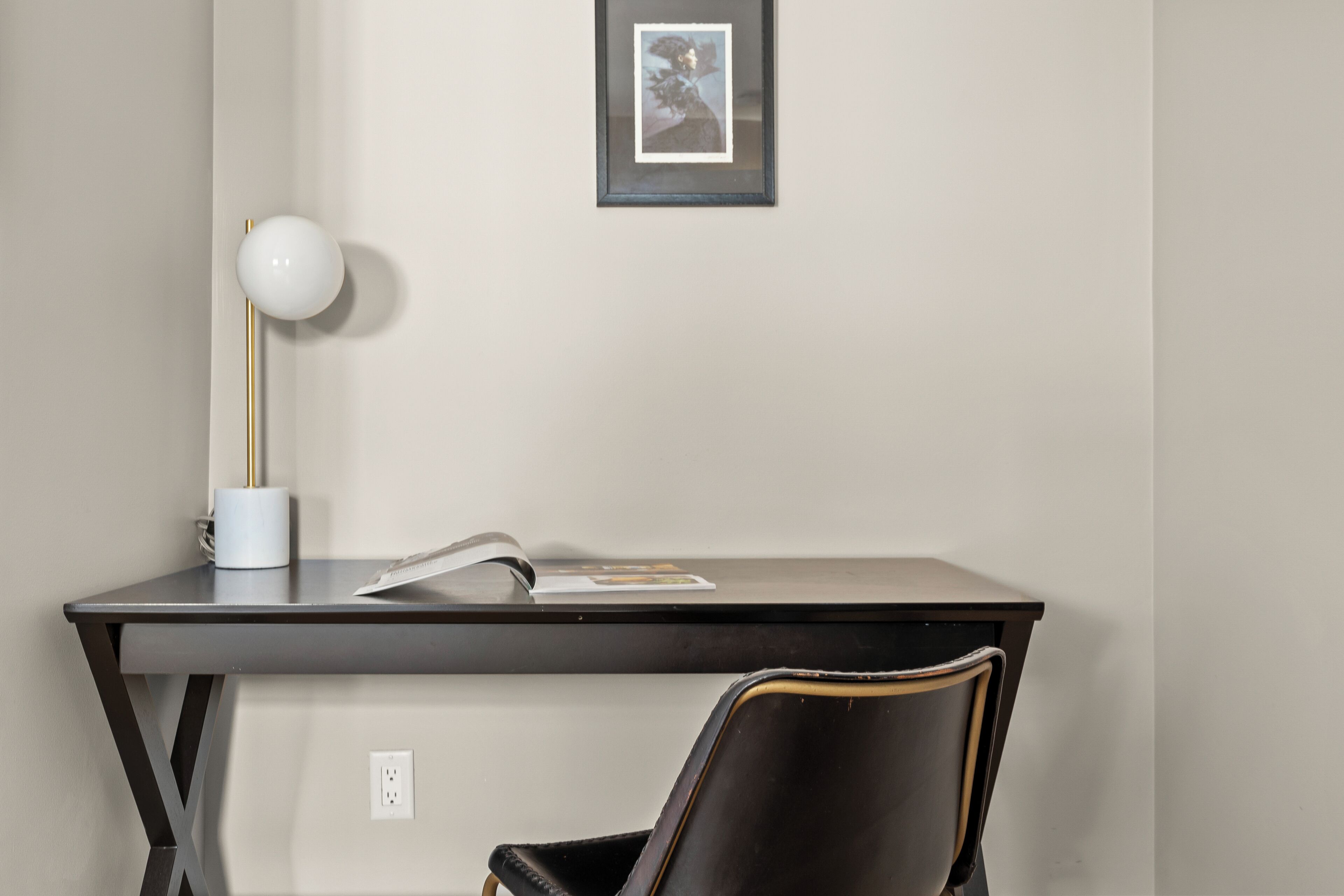 A desk with a lamp, a chair, and a framed picture on the wall.