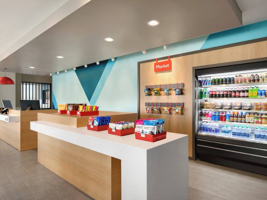 Un área de recepción moderna con mostrador, un letrero que dice 'Market' y un refrigerador con bebidas.