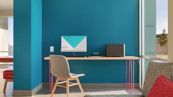 A modern office space with teal walls, a desk with a computer, a chair, and a couch with a red pillow.