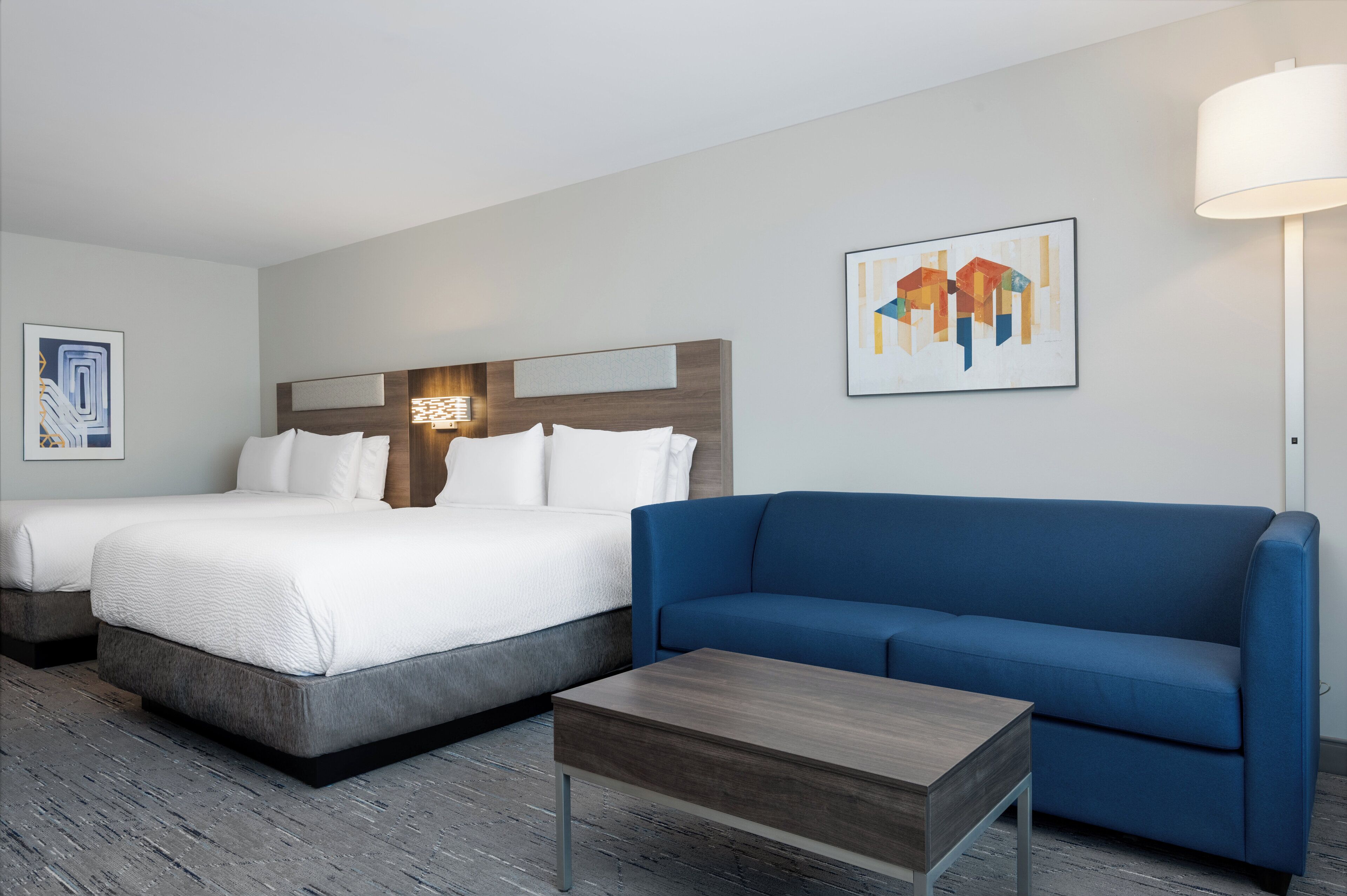 A hotel room with two beds, a blue sofa, a wooden coffee table, and artwork on the walls.