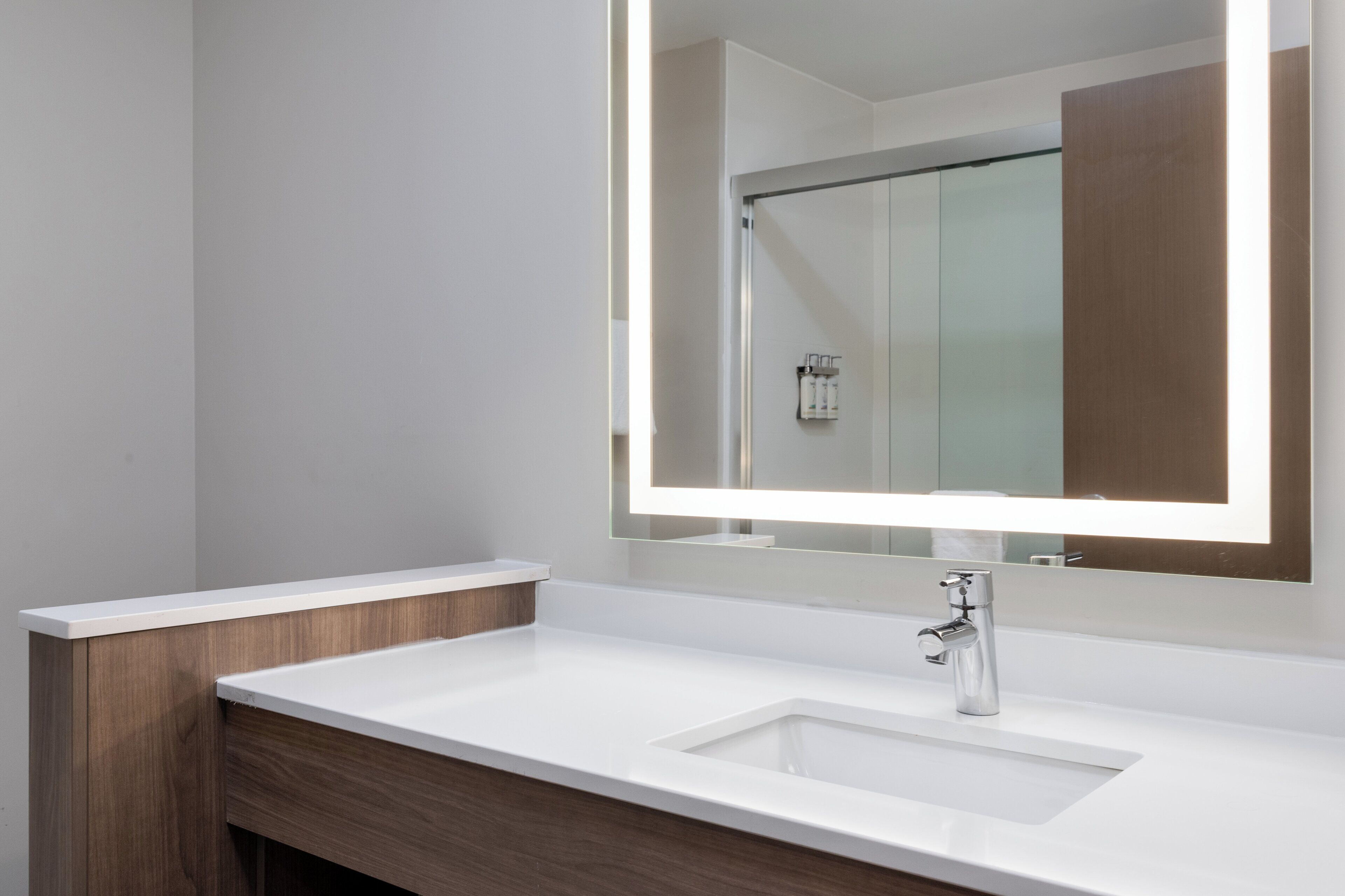 A modern bathroom with a white sink, a mirror with integrated lighting, and a wooden vanity.