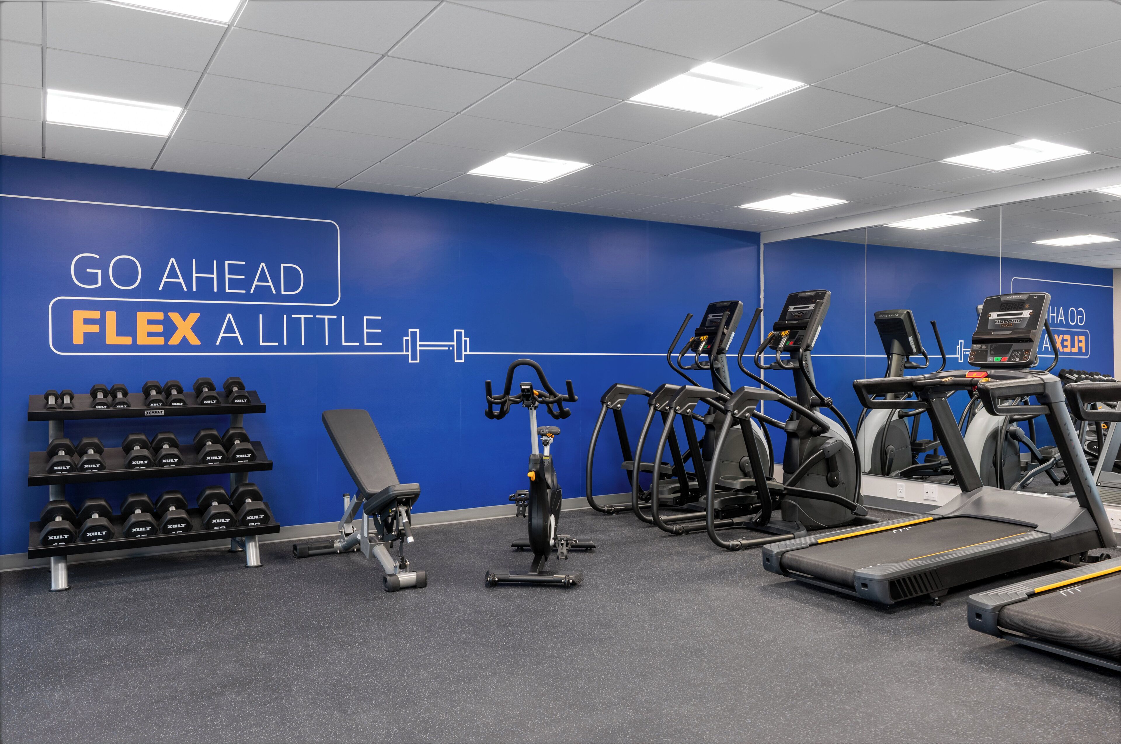 Une salle de sport équipée de tapis de course, de vélos elliptiques et d’un banc de musculation.