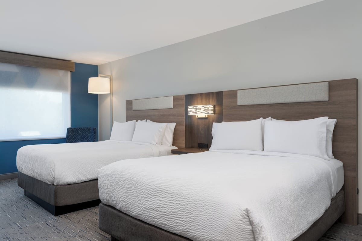 A hotel room with two beds, a large window, and a modern wall design.