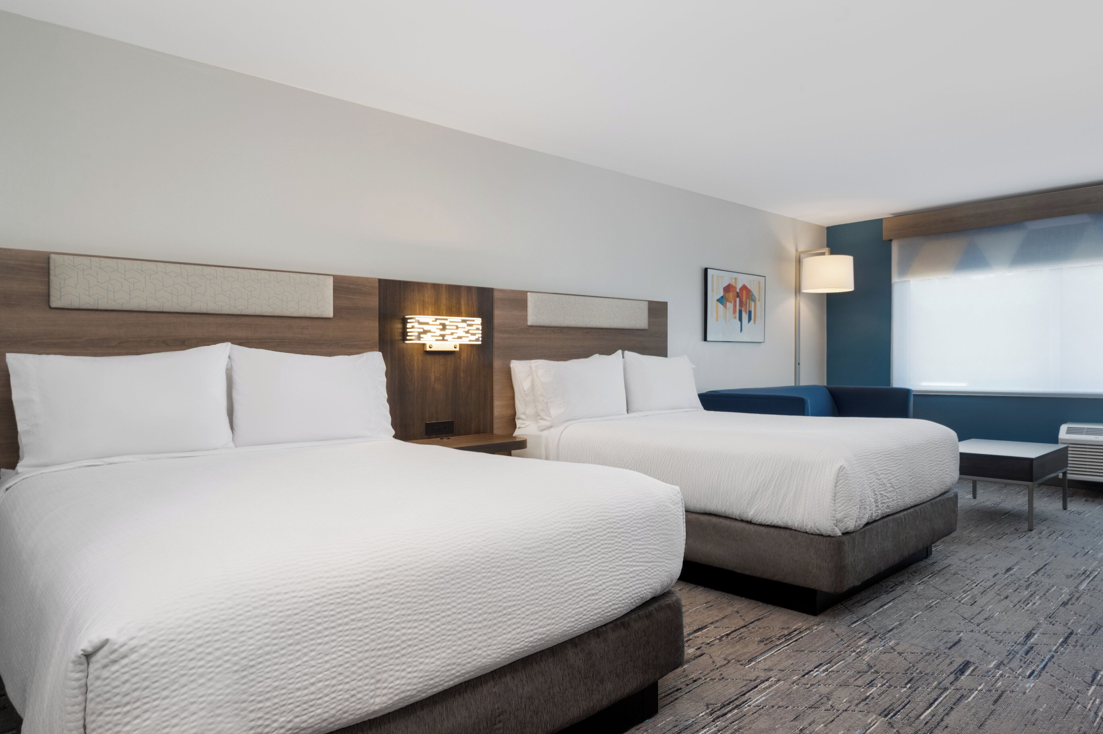 A hotel room with two beds, a desk, and a chair.