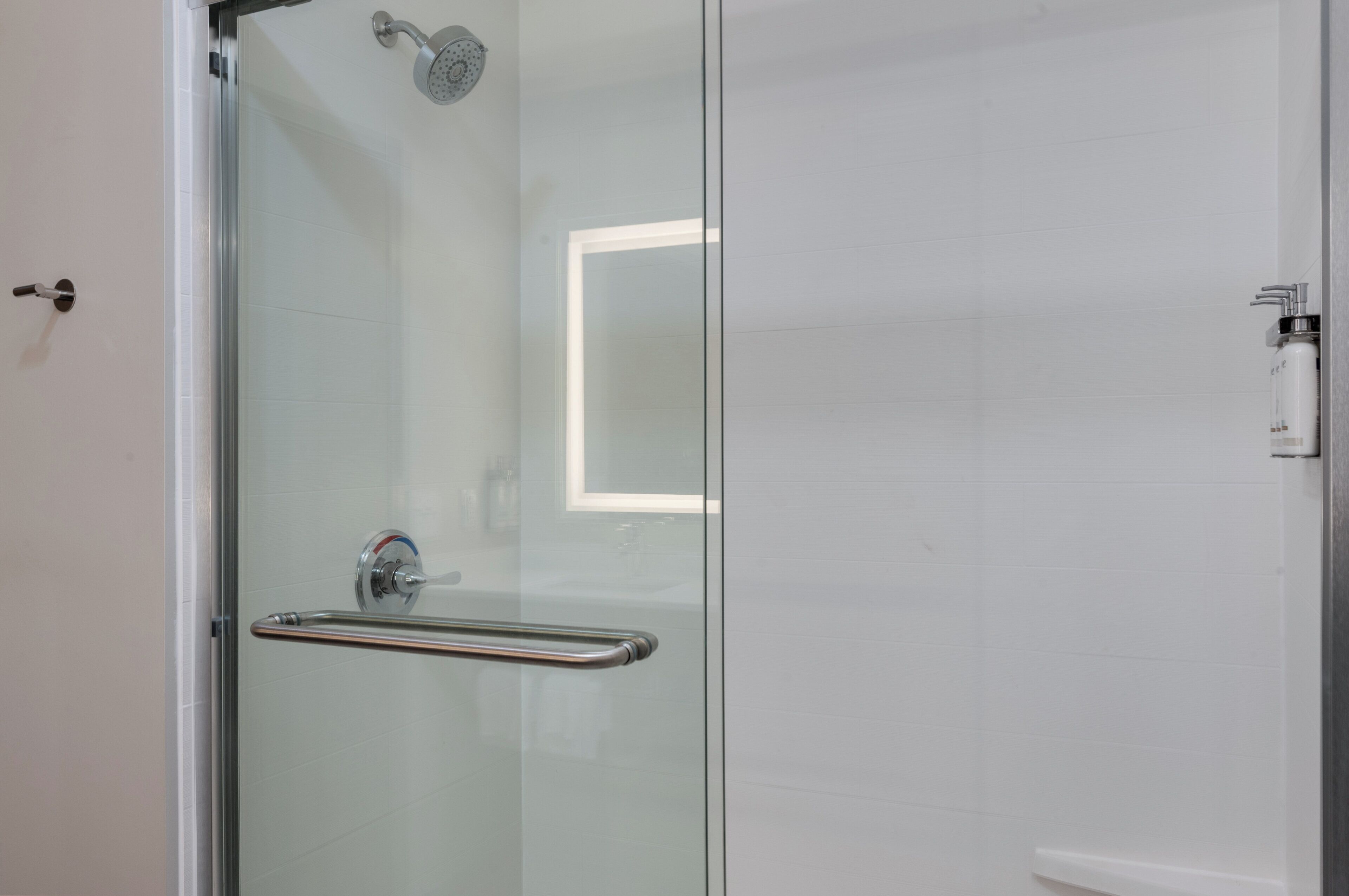 A glass-enclosed shower with a handheld showerhead, a glass door with a handle, and a small mirror on the wall.