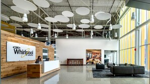 A modern reception area with a wooden reception desk, a large sign for Whirlpool Corporation, and a seating area with a sofa and chairs.