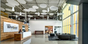 A modern reception area with a wooden reception desk, a large sign for Whirlpool Corporation, and a seating area with a sofa and chairs.