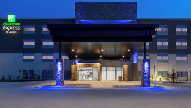 A Holiday Inn Express & Suites building with a modern design, featuring a large entrance with glass doors, stone pillars, and a blue-lit facade.