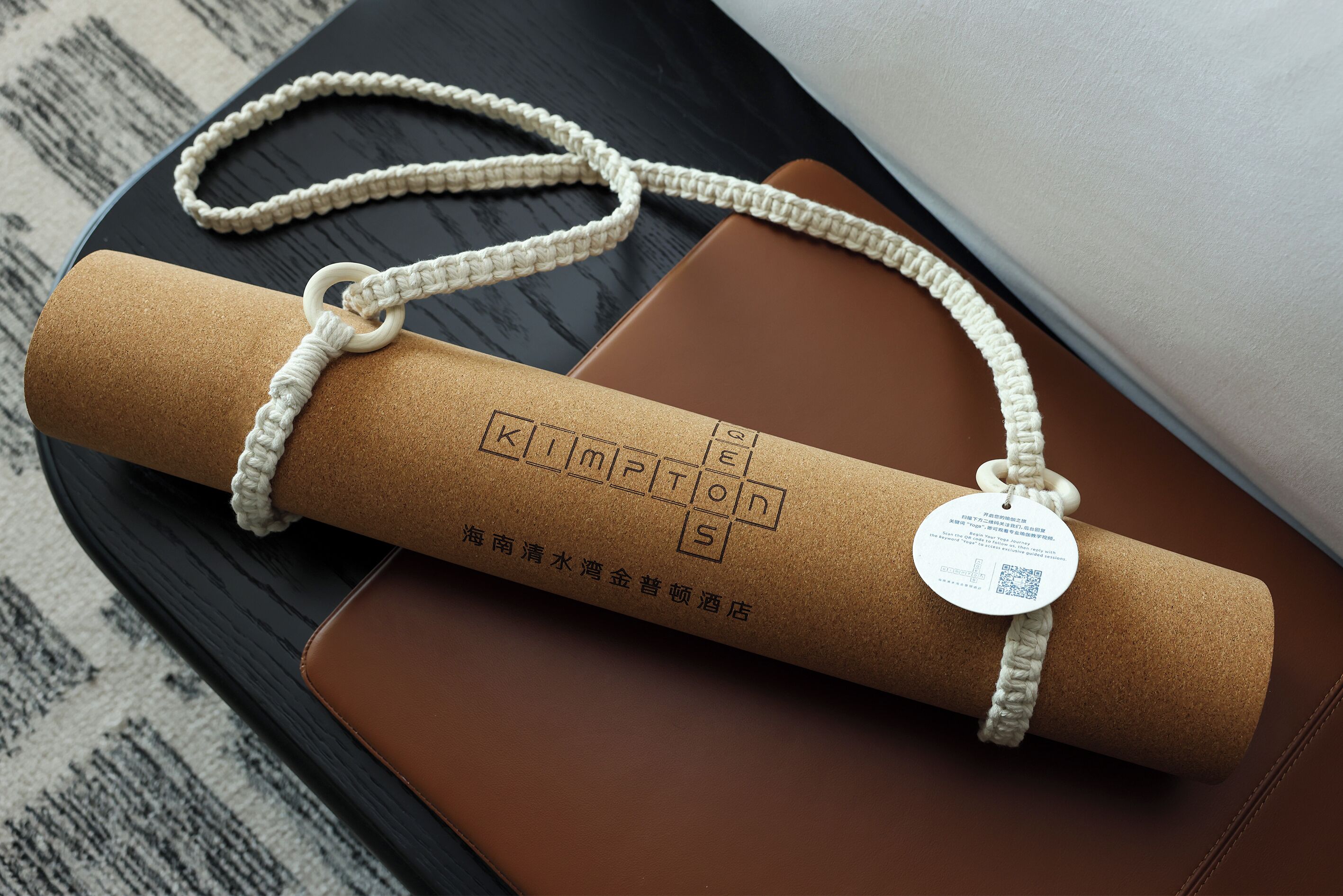 A rolled-up brown leather item with a white braided cord and a tag, placed on a black and brown surface.
