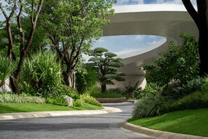 A pathway leading to a modern building with a curved roof, surrounded by lush greenery and trees. - Kimpton Aqeos Hainan by IHG (Lingshui)