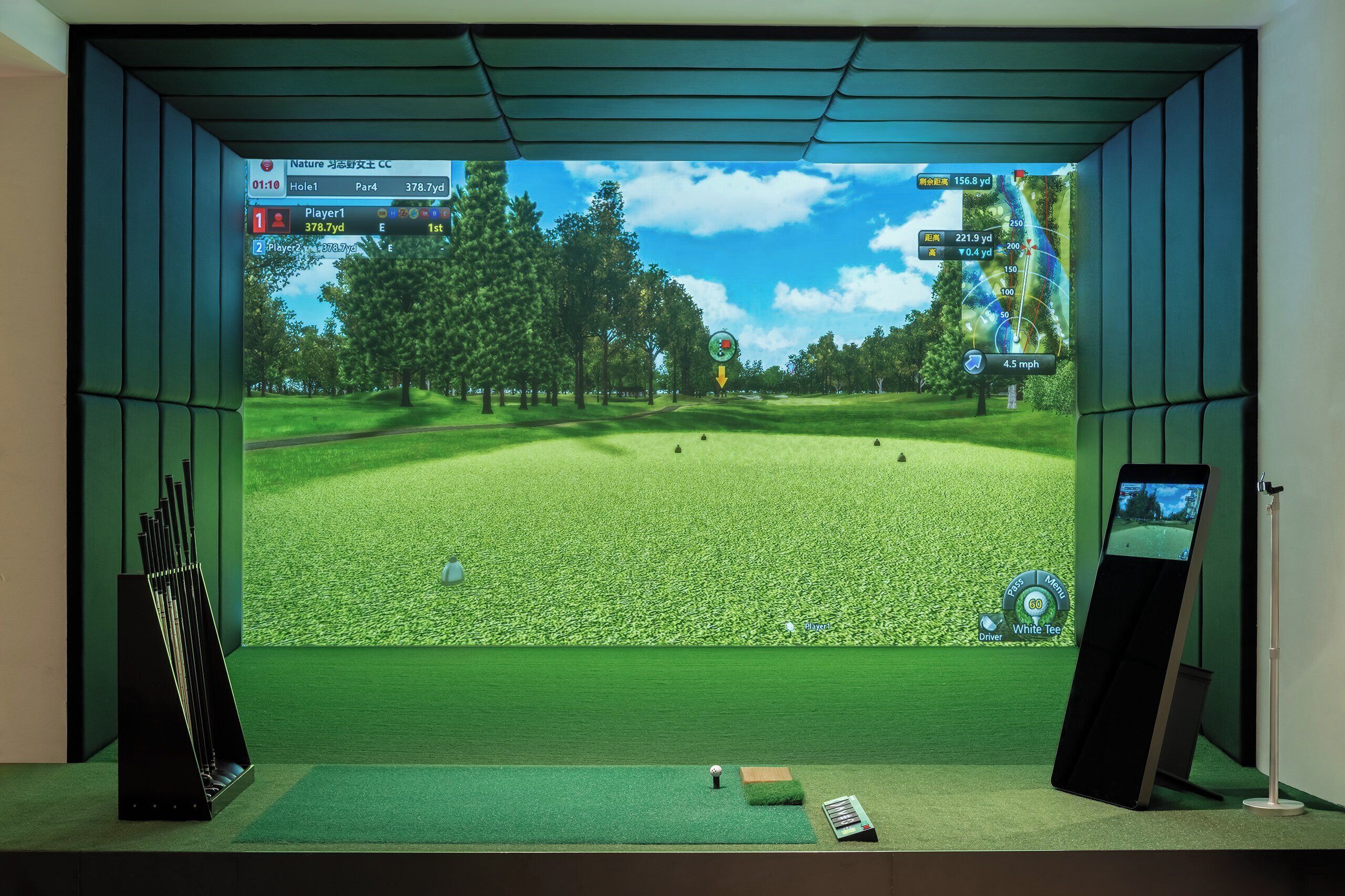 Configuración de simulación de golf con una pantalla mostrando un campo de golf, un soporte para palos de golf y una pelota en un tapete.