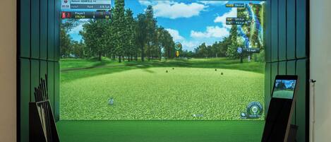 Configuración de simulación de golf con una pantalla mostrando un campo de golf, un soporte para palos de golf y una pelota en un tapete.