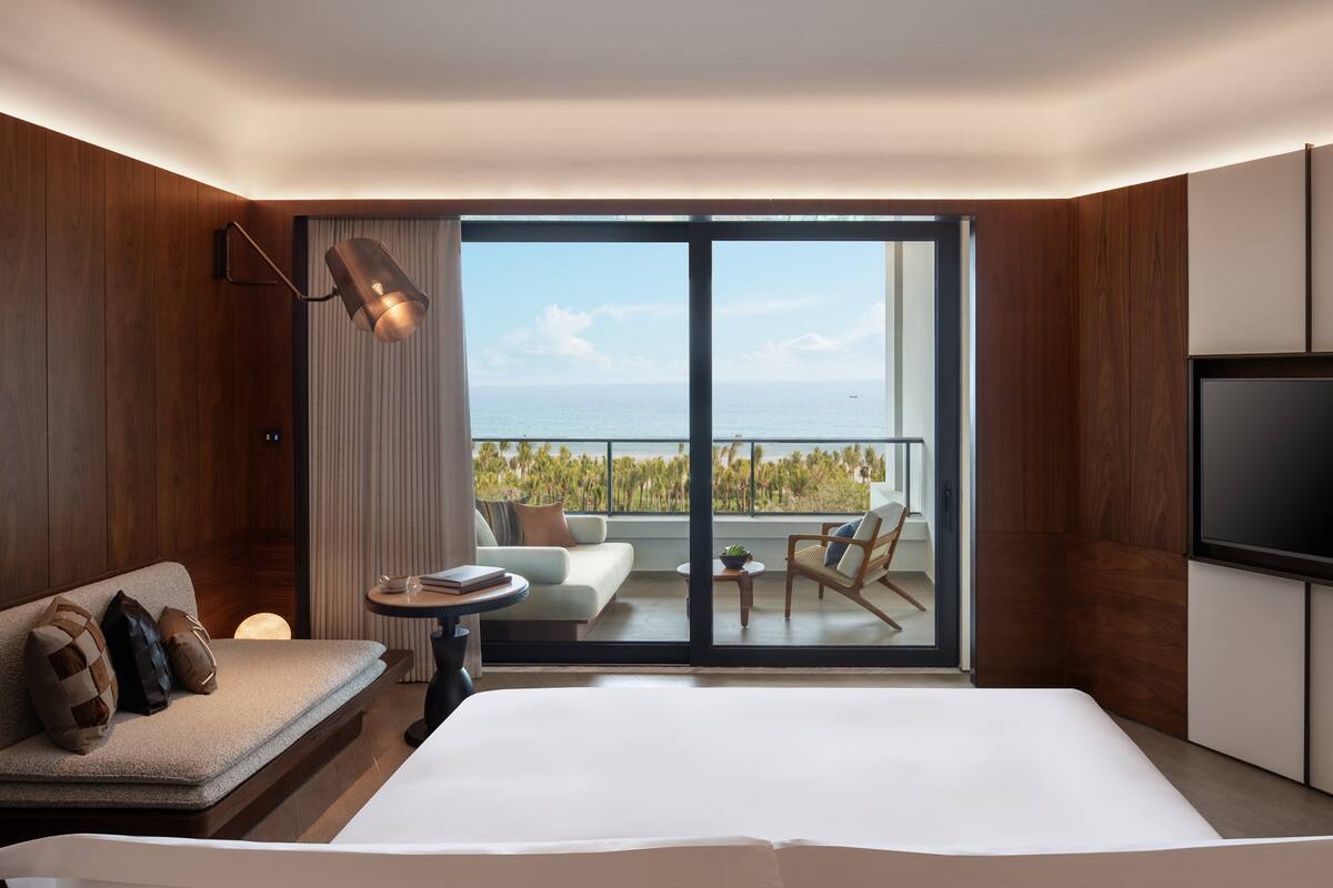 A modern hotel room with a large bed, a sofa, a TV, and a balcony with a view of the sea.