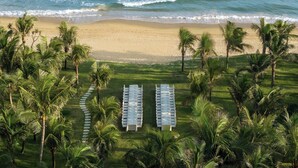 An aerial view of a beach with a row of white tables and chairs, surrounded by palm trees and ocean waves. - Kimpton Aqeos Hainan by IHG (Lingshui)