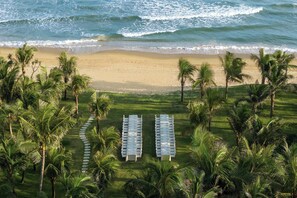 An aerial view of a beach with a row of white tables and chairs, surrounded by palm trees and ocean waves. - Kimpton Aqeos Hainan by IHG (Lingshui)