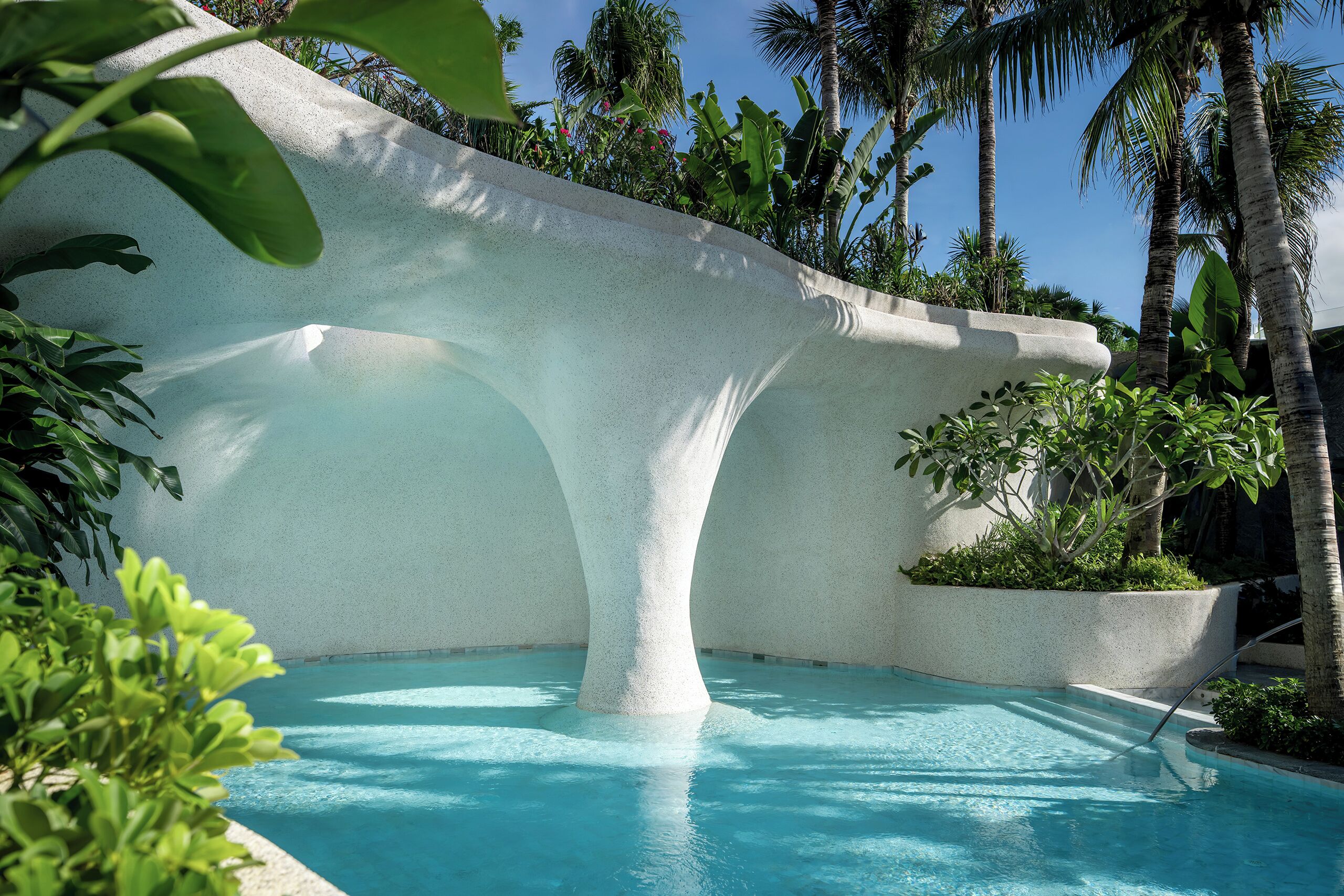 A pool with a unique architectural design, surrounded by lush greenery and palm trees.