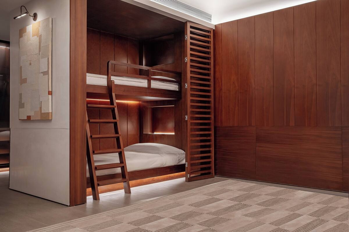 A room with a bunk bed, wooden wardrobe, and a small desk with a chair.