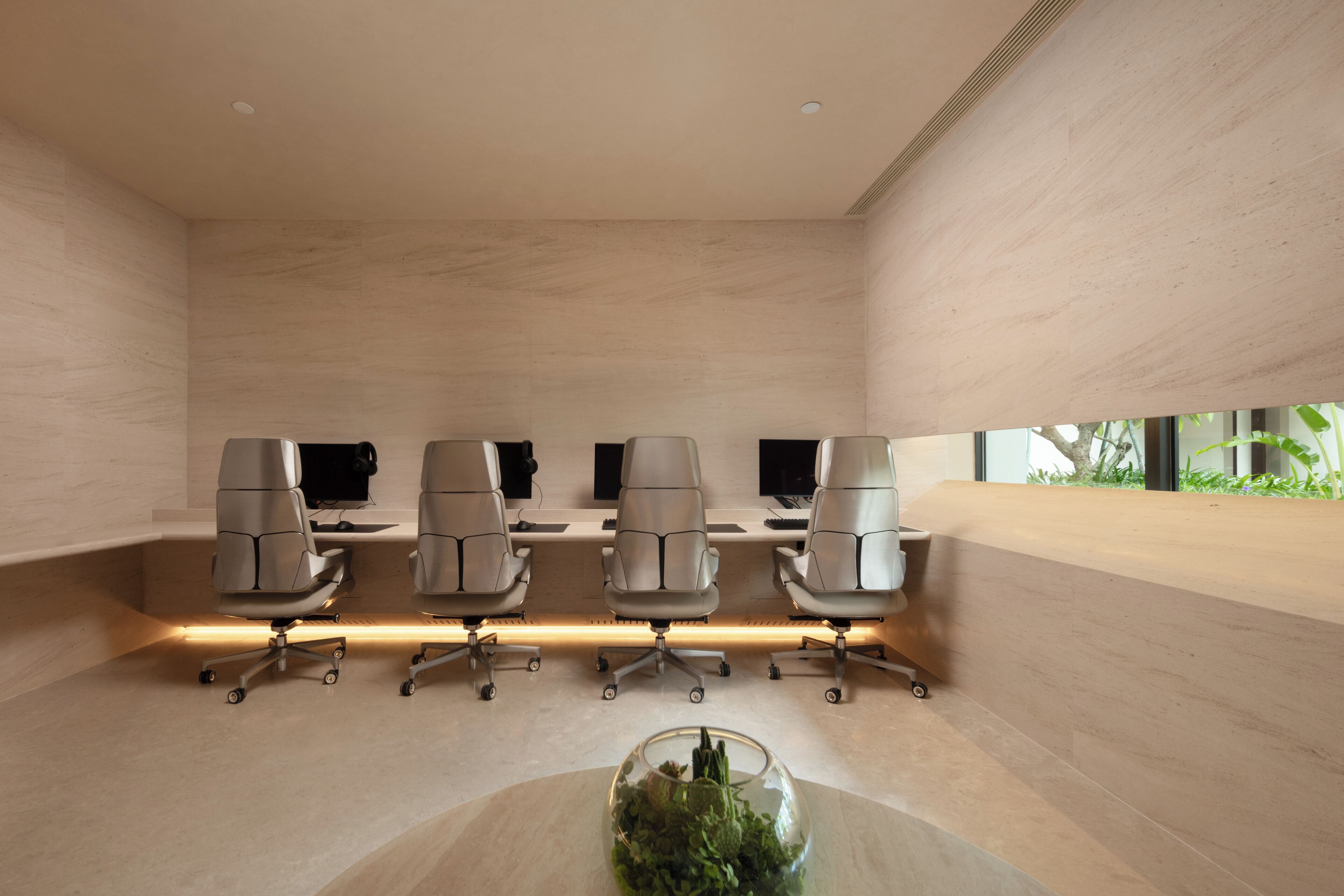 Un salón de conferencias con cinco sillas ergonómicas, una mesa de cristal con plantas y un diseño moderno que incluye una pared y techo de color claro.