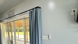 A room with a wooden floor, a sliding glass door leading to an outdoor area, and a wall-mounted electrical outlet. - Magnolia Estate Container Home (Sardis)