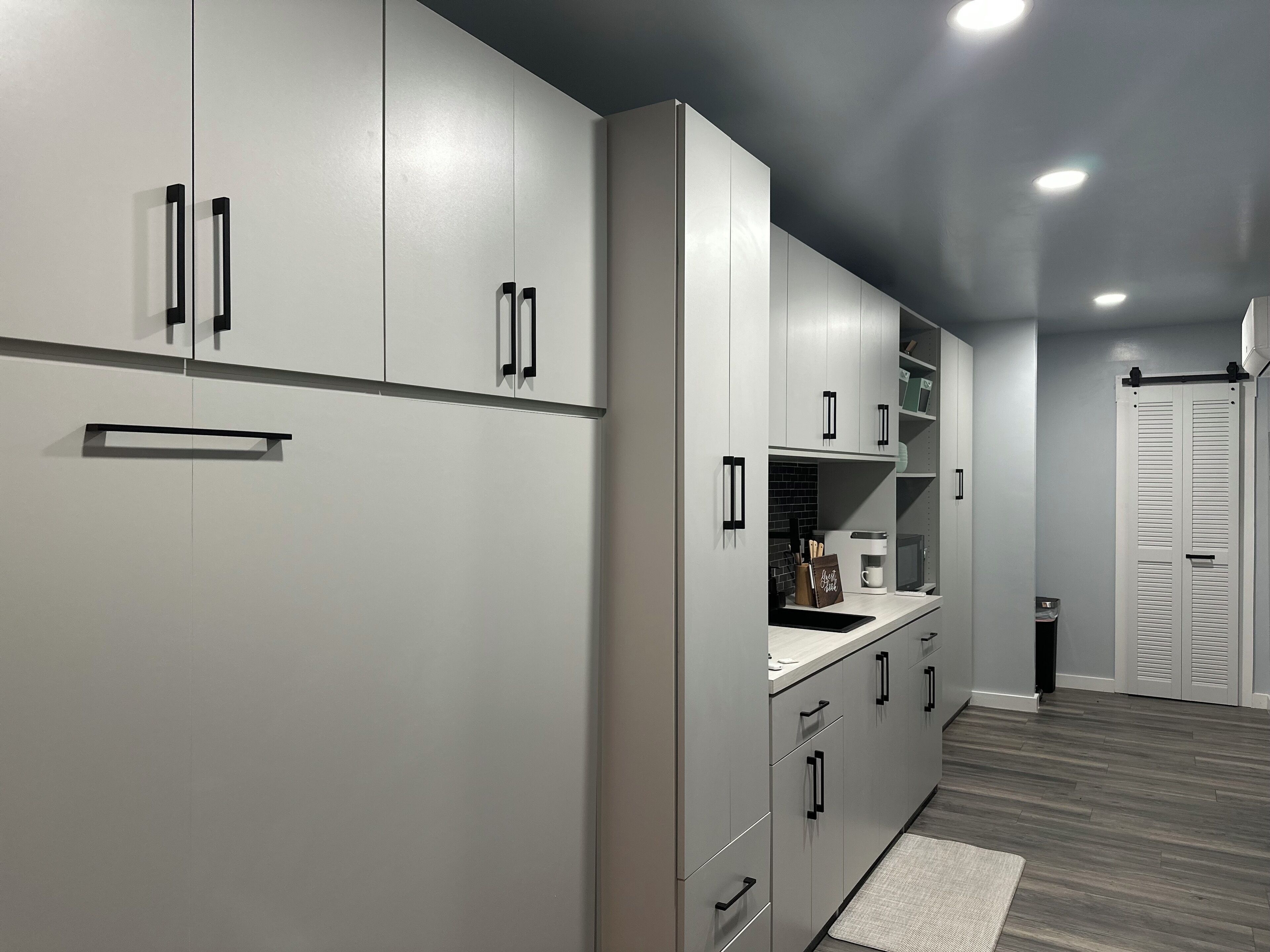Une cuisine moderne avec des meubles gris, des poignées noires et un plancher en bois.