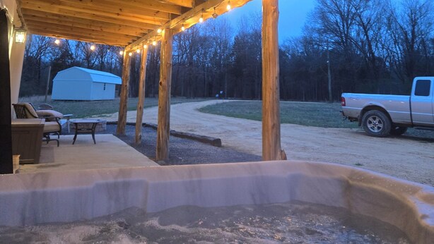 A covered outdoor area with a hot tub, wooden beams, and string lights. - Magnolia Estate Container Home (Sardis)
