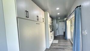 A modern kitchen with white cabinets, a wooden floor, and a ceiling light. - Magnolia Estate Container Home (Sardis)