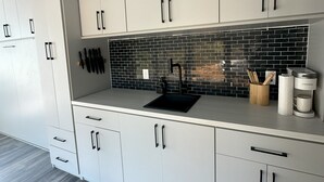 A modern kitchen with white cabinets, a black backsplash, and a stainless steel sink. - Magnolia Estate Container Home (Sardis)
