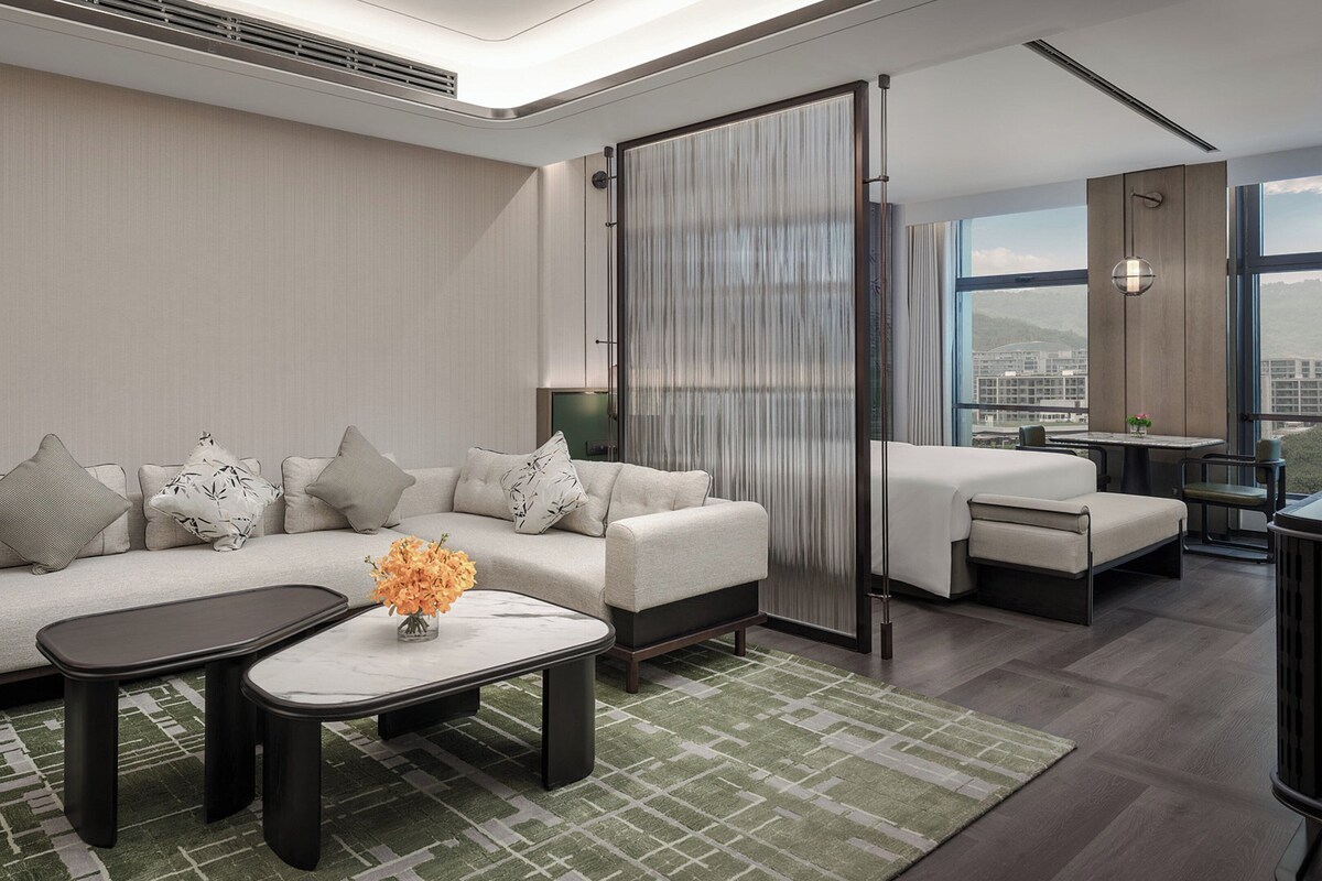 A modern living room with a sofa, coffee table, and a view of the city through large windows.